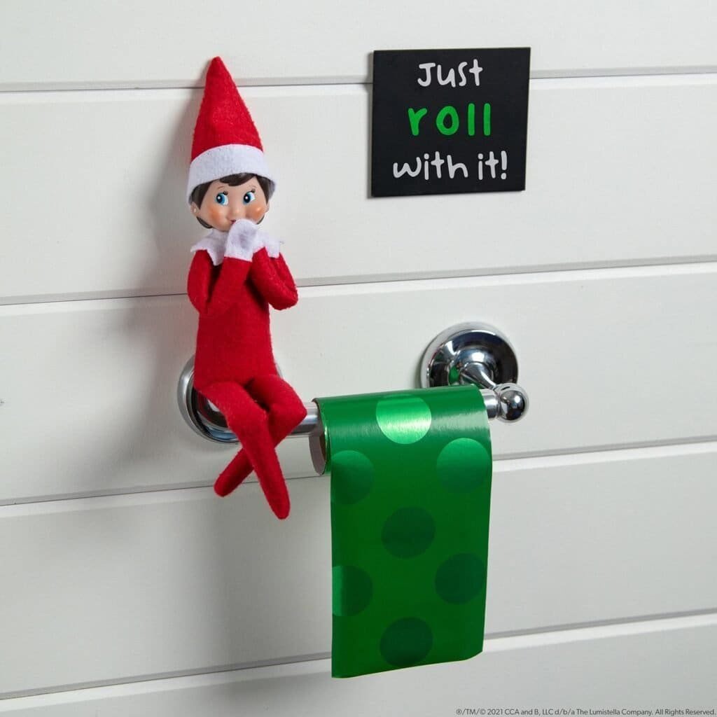 Elf on the Shelf sitting next to a roll of gift wrap as toilet paper, showcasing a funny holiday twist for Elf on the Shelf ideas.