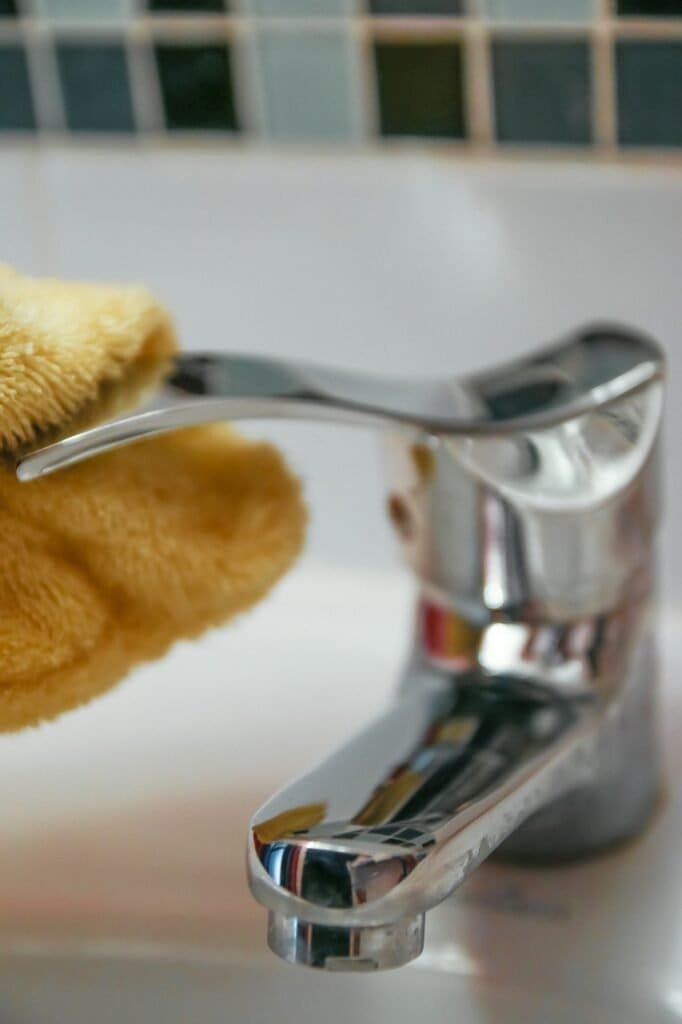 Cleaning a faucet as part of bathroom floor maintenance.